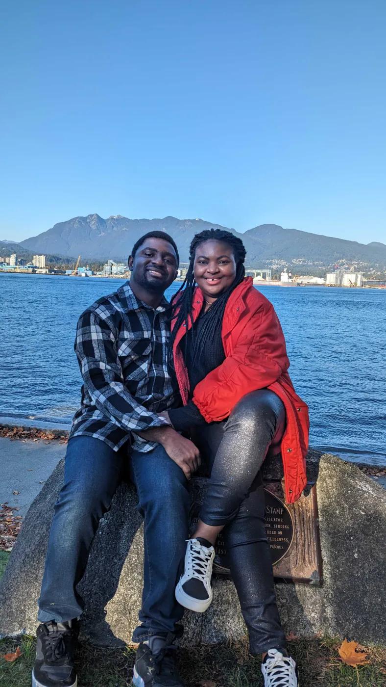 Francis with another person by the water with mountains behind them